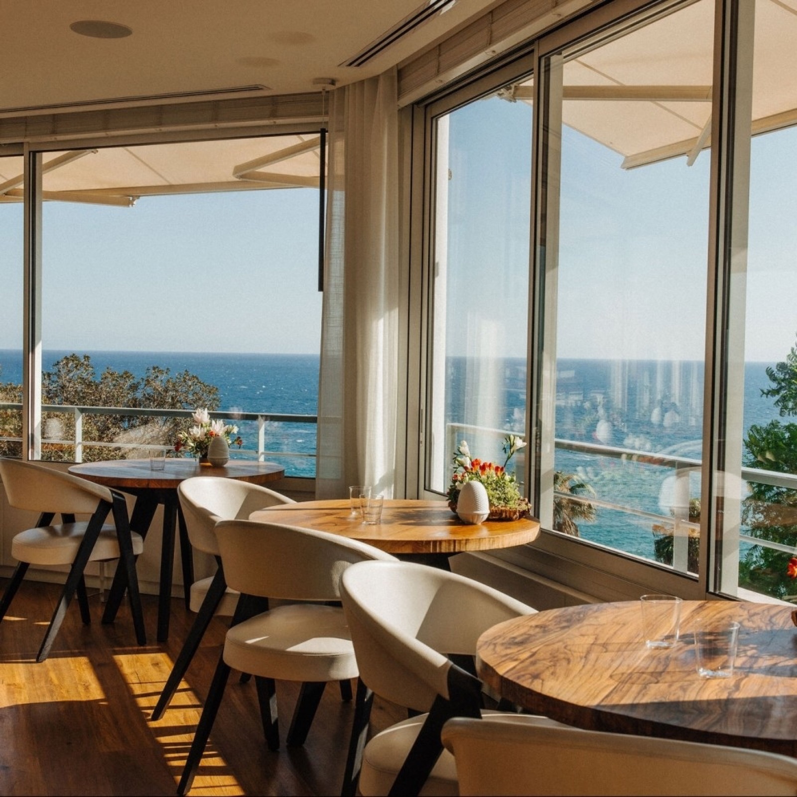 Salle du Mirazur avec baies vitrées vue mer, tables rondes, fauteuils blancs design