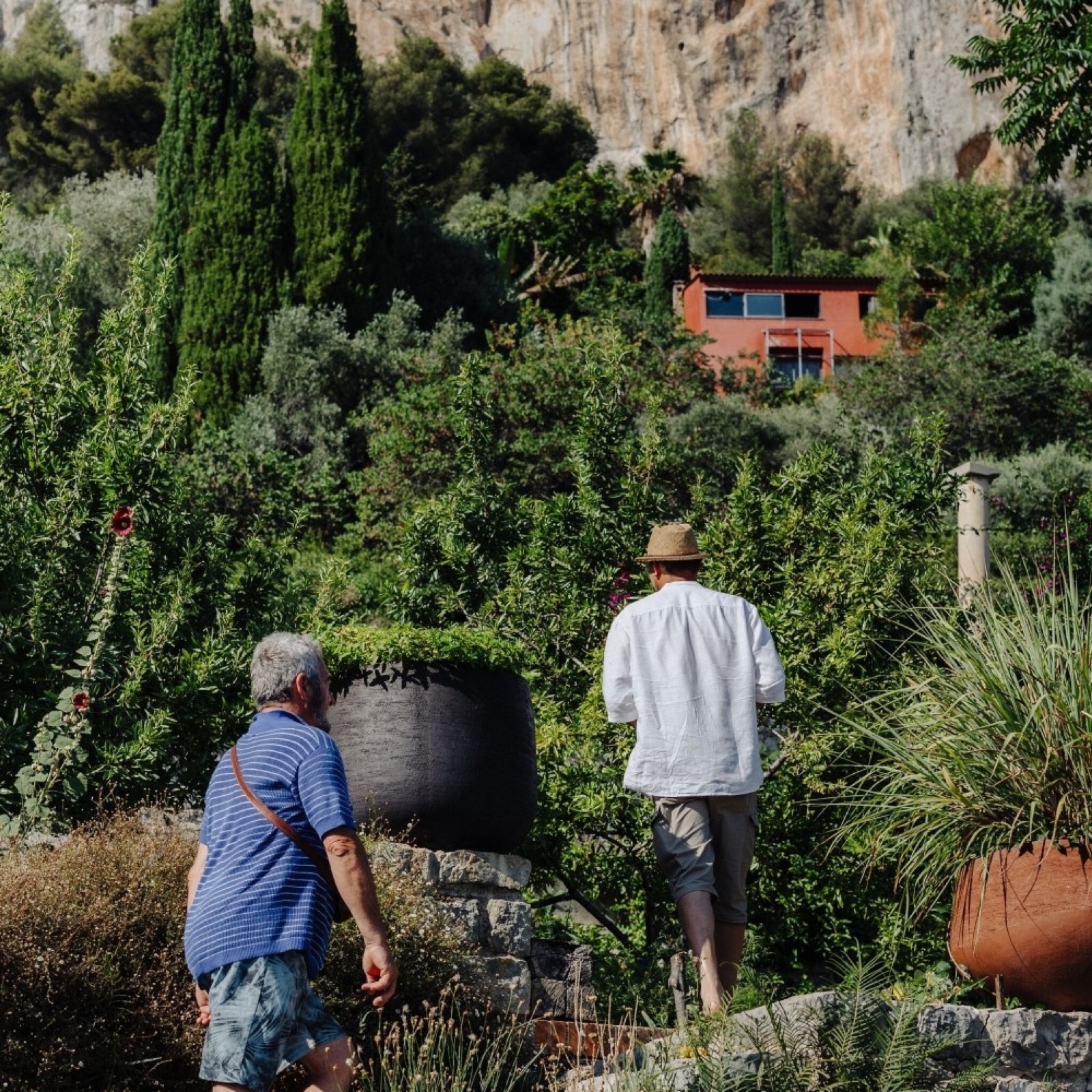 Jardin Castillon avec maison ocre rouge, terrasses et oliviers, deux personnes en visite