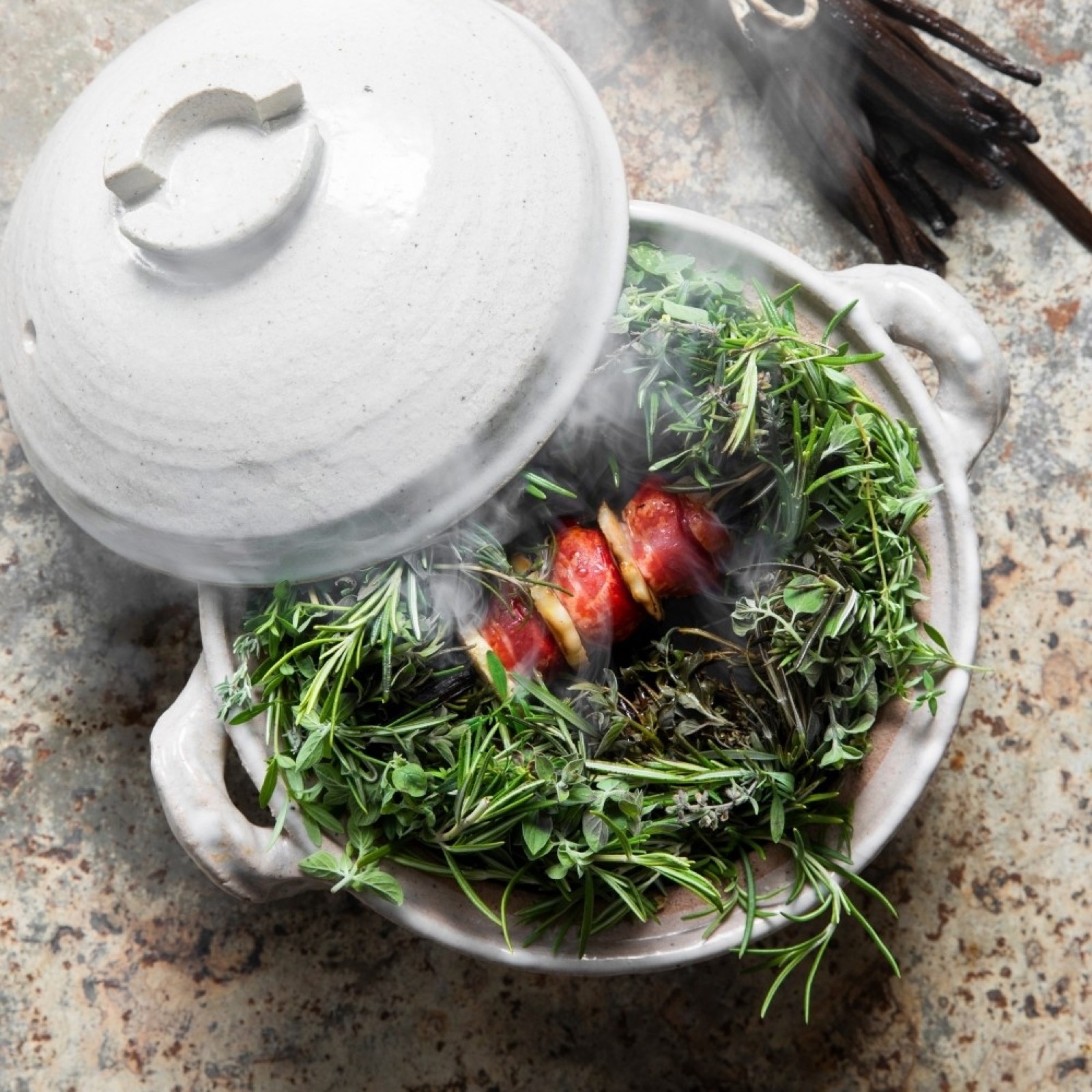 Cocotte céramique entrouverte avec vapeur, lit d'herbes et racines — univers Racine