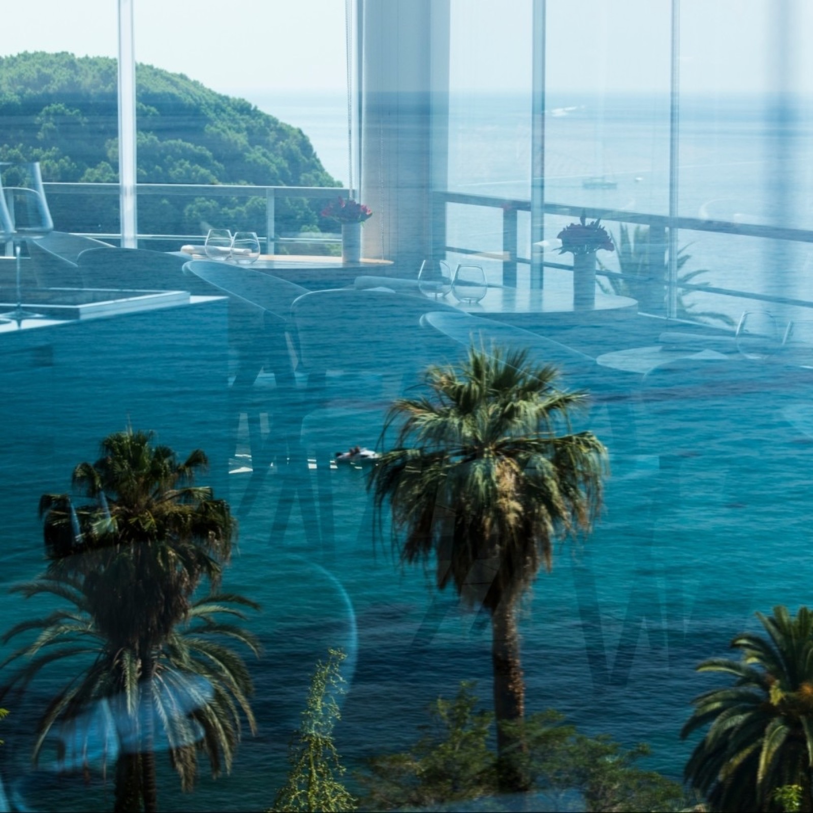 Vue depuis la salle du Mirazur à travers les baies vitrées : palmiers et mer Méditerranée
