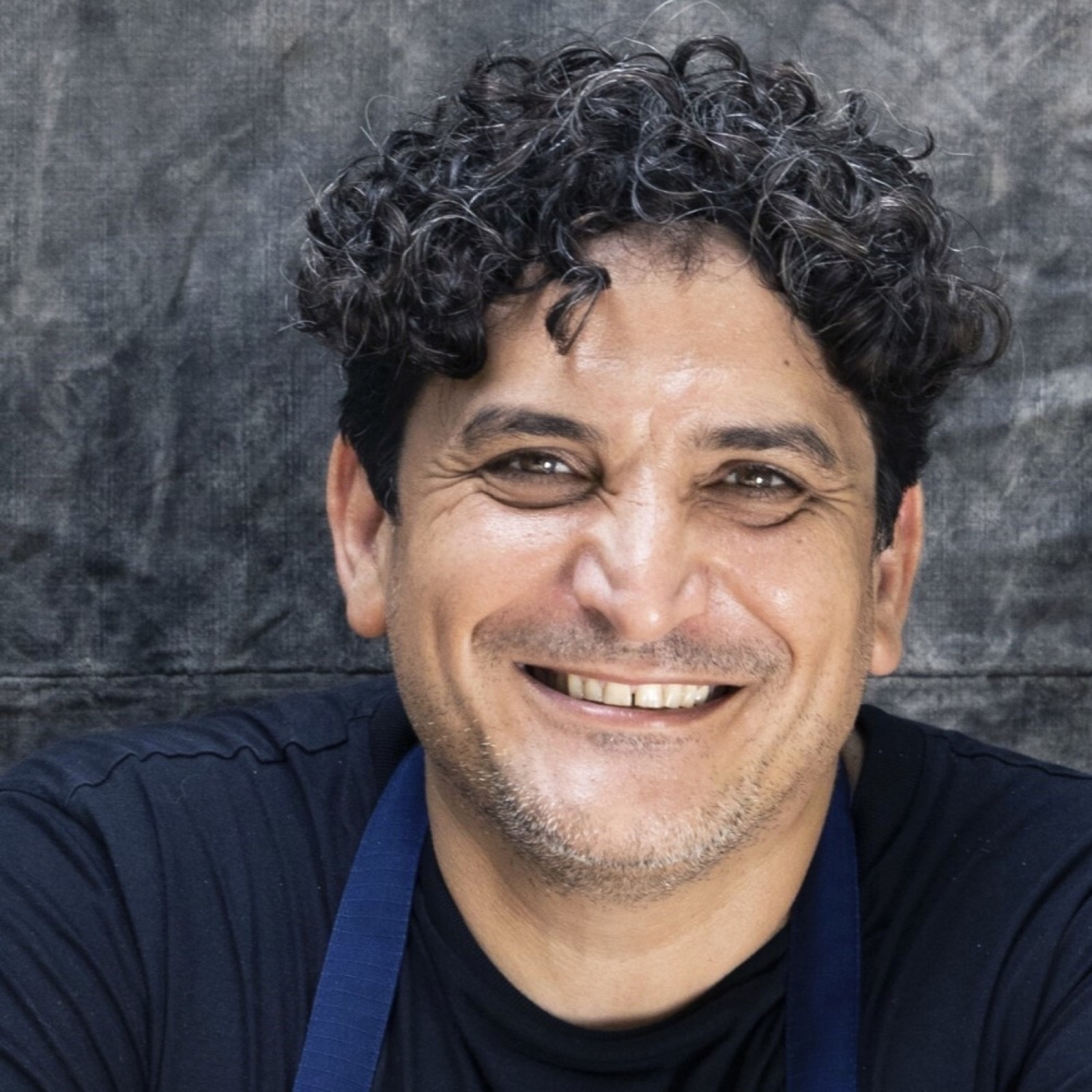 Portrait studio de Mauro Colagreco, chef-propriétaire du Mirazur, tablier marine sur t-shirt noir